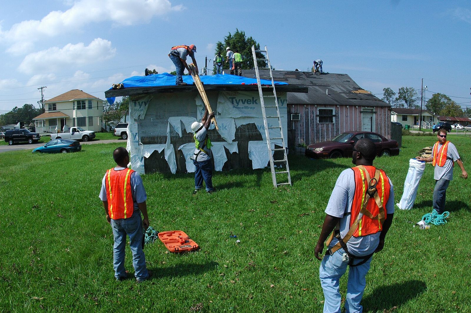 Crew fastening a blue tarp over a roof after a hurricane